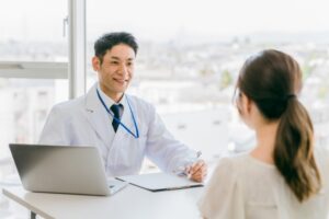 白衣の男性がPCと資料を用いて女性に説明しているところ。カウンセリング。
